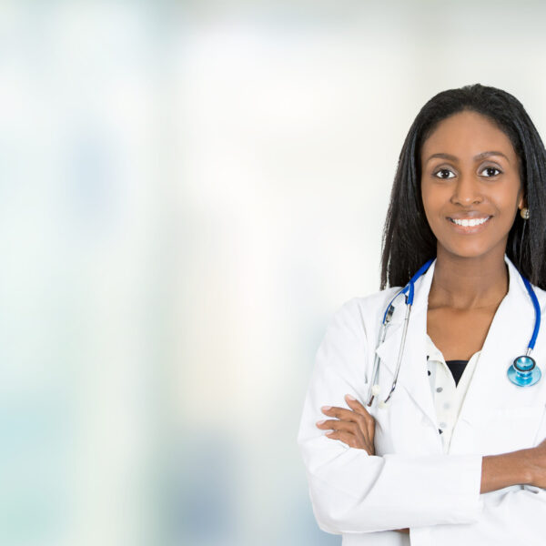 Portrait confident African American female doctor medical professional standing isolated on hospital clinic  hallway windows background. Positive face expression